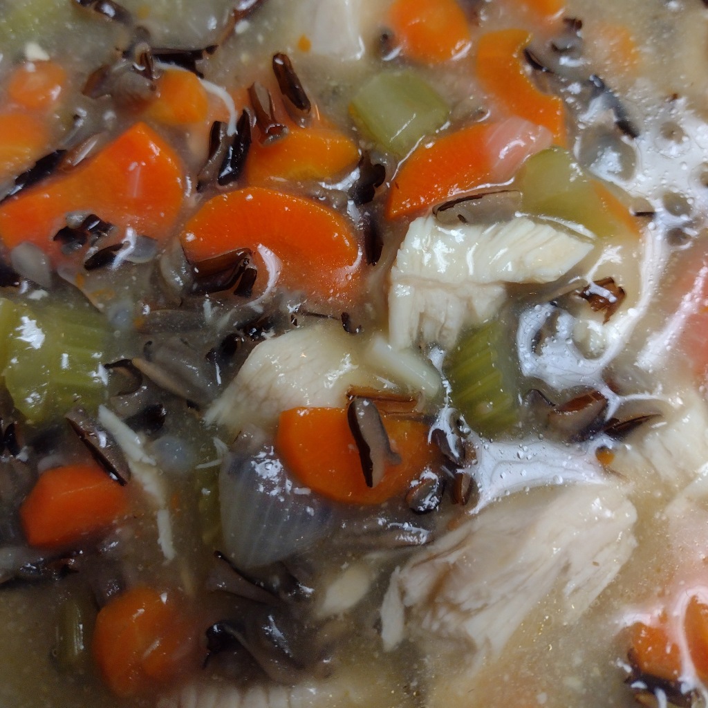 a close up of the chicken, carrots, celery, onions, wild rice, and thickened broth in the cooked dish